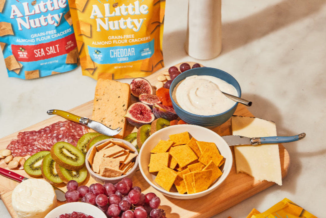 Snack platter with 'A Little Nutty' crackers, fruits, and cheese on a wooden board.