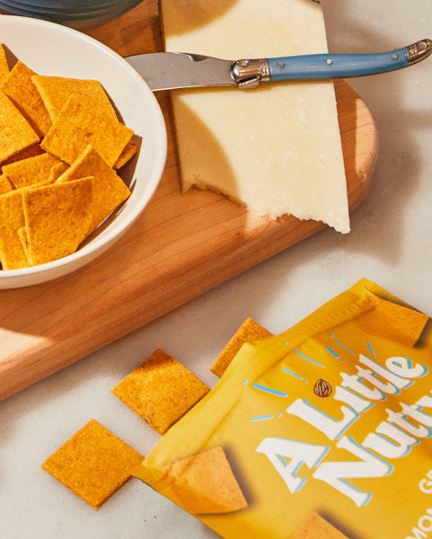 Assorted snacks including cheese, crackers, and fruits on a wooden board with Little Nutty packaging.
